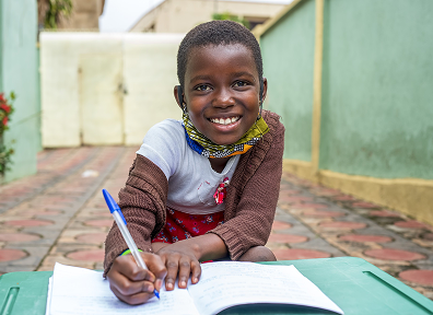 A smiling girl writing in an exercise book outdoors
